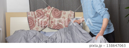 A 53-year-old man is actively changing the bed linen in his bedroom. He is focused on putting fresh sheets on the bed, demonstrating a common home chore, banner 138647063