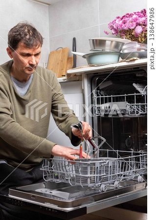 A man stands in his kitchen taking clean dishes out of the dishwasher. He focuses on the process of unloading the clean dishes and organizing them for use 138647986