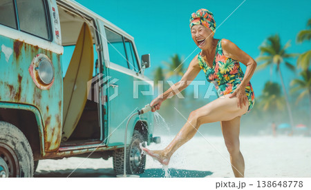 A woman stands near a vintage van at a tropical beach. She laughs as she splashes water on her feet. The sky is clear and the palm trees sway in the breeze. 138648778