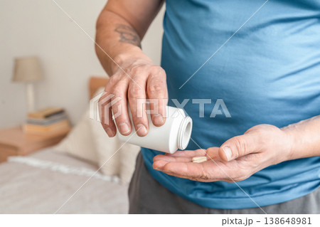 Man holding a white bottle, pouring two capsules onto his open palm, symbolizing health and wellness. Taking care of your health and disease prevention Man holding a white bottle, pouring two capsules onto his open palm, symbolizing health and wellness. Taking care of your health and disease prevention 138648981