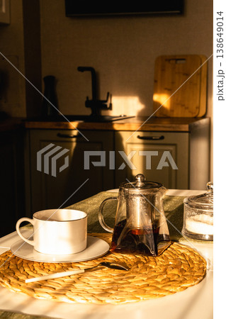 Cozy morning tea ritual: glass teapot, cup and sugar bowl on a sunlit kitchen table, warm golden-hour light and calm domestic charm. Tea time table setup for a cozy tea party at home Cozy morning tea ritual: glass teapot, cup and sugar bowl on a sunlit kitchen table, warm golden-hour light and calm domestic charm. Tea time table setup for a cozy tea party at home 138649014