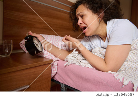 Overslept woman holding a black alarm clock, she's shocked after wake up too late for appointment or work Overslept woman holding a black alarm clock, she's shocked after wake up too late for appointment or work 138649587