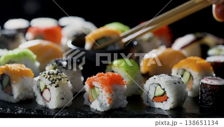 Sushi being served on a dark plate with chopsticks picking up a piece in a lively restaurant setting Sushi being served on a dark plate with chopsticks picking up a piece in a lively restaurant setting 138651134