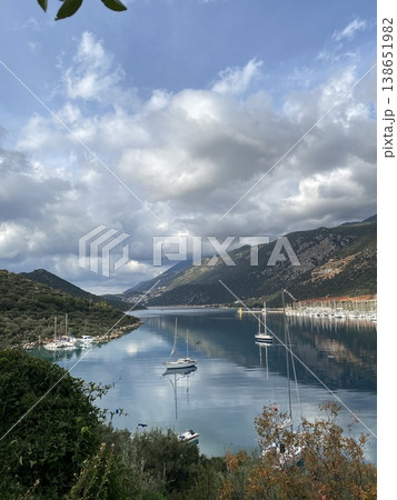 Scenic view of sailboats anchored in a calm bay surrounded by mountains and reflected clouds Scenic view of sailboats anchored in a calm bay surrounded by mountains and reflected clouds 138651982
