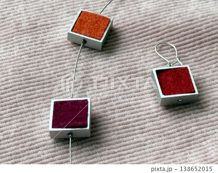 Geometric jewelry on textured pink fabric background, featuring squares with vibrant colors Geometric jewelry on textured pink fabric background, featuring squares with vibrant colors 138652015