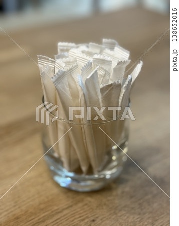 Sugar packets arranged neatly in a clear glass on a wooden table, use as background Sugar packets arranged neatly in a clear glass on a wooden table, use as background 138652016