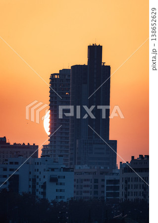 Sun Setting Behind a Tall Building with Orange Hues 138652629