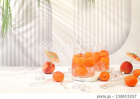Iced peach tea or cocktail with mint and apricots, refreshing summer drink recipe. Two glasses with peach fruit lemonade on a light table, detox diet and weight loss concept, restaurant menu, 138653207