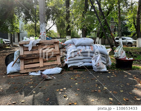 Bags of construction materials are stacked and pallets are piled in a city yard or park. 138653433