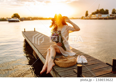 Young woman in dress sitting on wooden pier near pond. Rustic style of wedding. Travel, tourism 138653622