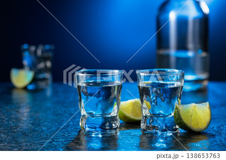 Vodka with lime slices on a black stone table. 138653763