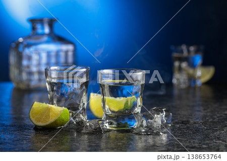 Vodka with lime slices on a black stone table. 138653764