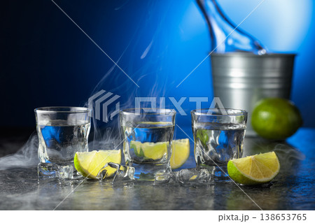 Vodka with lime slices on a black stone table. 138653765