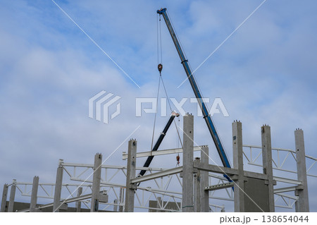 Crane lifting steel beam onto concrete columns at industrial construction site under cloudy sky Crane lifting steel beam onto concrete columns at industrial construction site under cloudy sky 138654044