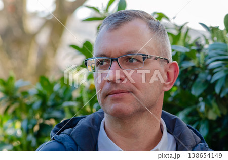 Portrait of man wearing glasses outdoors with green plants in soft natural light 138654149