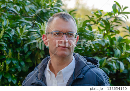 Portrait of man wearing glasses outdoors among dense greenery in soft natural light on warm day 138654150