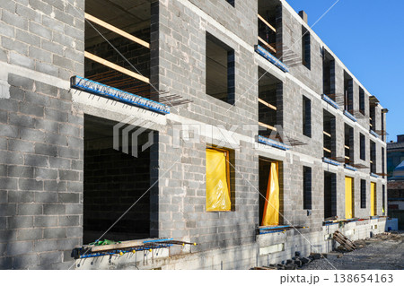 Concrete block apartment building under construction with open windows and yellow protective covers Concrete block apartment building under construction with open windows and yellow protective covers 138654163