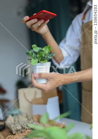 A shop owner or employee using phone checking order or to document the plant for inventory. 138654283