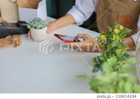 A shop owner or employee using phone checking order or to document the plant for inventory. 138654284