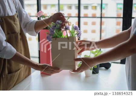 A florist or shop owner, handing a paper bag containing flowers to a customer.Flower shop, small business, retailing concept. 138654325
