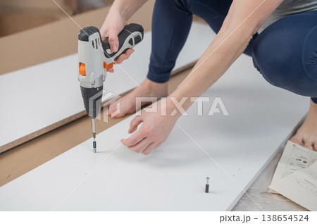A Caucasian woman uses a screwdriver to tighten a screw while assembling a cabinet. 138654524