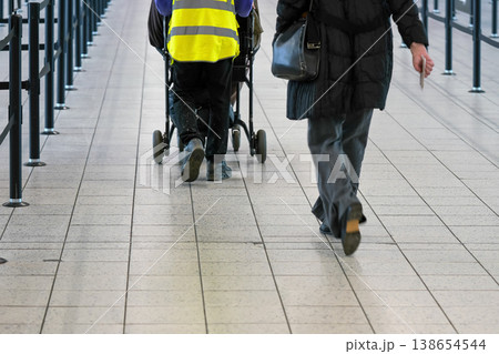 Passenger walking to airport departure gate, assistance staff helping with person on wheel chair, view from behind 138654544