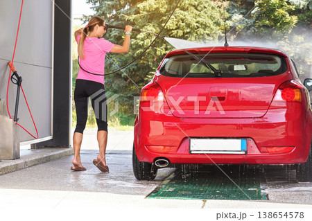 Young woman washing her red car in self serve carwash, view from back Young woman washing her red car in self serve carwash, view from back 138654578