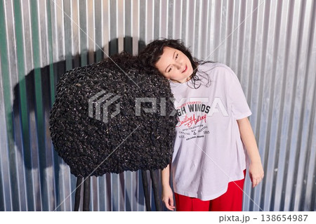 Model leans calmly before rippled metal wall with striking shadows Model leans calmly before rippled metal wall with striking shadows 138654987