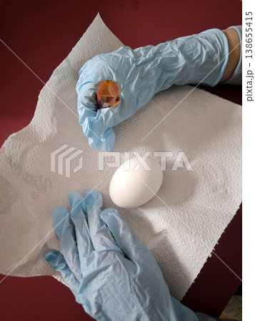 The process of dyeing a white egg with food coloring while wearing blue protective gloves The process of dyeing a white egg with food coloring while wearing blue protective gloves 138655415