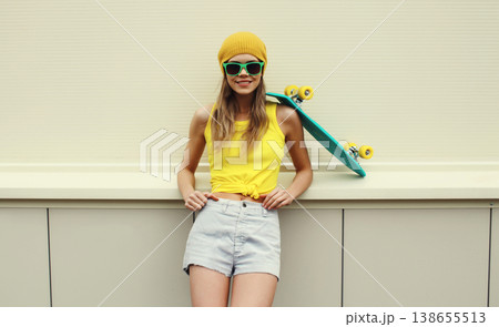 Stylish young woman with skateboard smiles, happy modern teenage girl posing on white wall 138655513