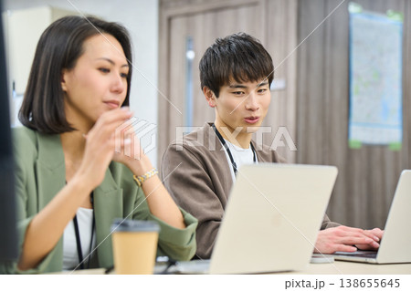 フリーアドレスのオフィスで女性の先輩に相談しながら作業する若い男性社員 フリーアドレスのオフィスで女性の先輩に相談しながら作業する若い男性社員 138655645