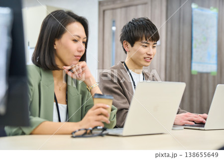フリーアドレスのオフィスで女性の先輩に相談しながら作業する若い男性社員 フリーアドレスのオフィスで女性の先輩に相談しながら作業する若い男性社員 138655649