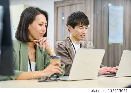 フリーアドレスのオフィスで女性の先輩に相談しながら作業する若い男性社員 フリーアドレスのオフィスで女性の先輩に相談しながら作業する若い男性社員 138655651