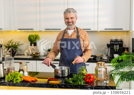 Middle-aged man cooking healthy soup on electric stove in home kitchen for diet nutrition lifestyle Middle-aged man cooking healthy soup on electric stove in home kitchen for diet nutrition lifestyle 138656221