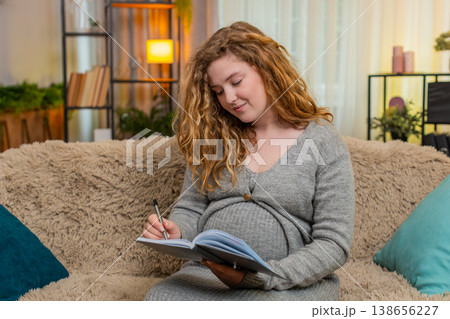 Pregnant young woman writing in diary to do list at home, thoughtful and focused, future planning 138656227