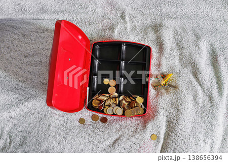 Open red cash box on textile bed blanket with scattered coins Open red cash box on textile bed blanket with scattered coins 138656394