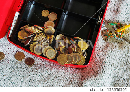 Open red cash box on textile bed blanket with scattered coins 138656395