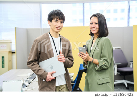 デバイスを持ちオフィスでカメラに微笑む外資系企業の若い男女 デバイスを持ちオフィスでカメラに微笑む外資系企業の若い男女 138656422