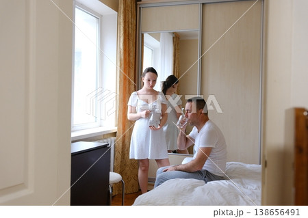 Teenage daughter pouring water for father at home cozy beige bedroom caring family moment weekend routine indoor lifestyle 138656491