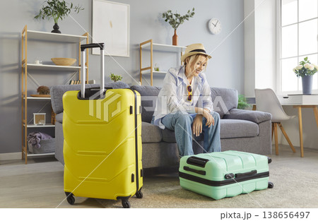 Happy young woman in beach hat sitting on sofa at home with suitcases ready for vacation trip Happy young woman in beach hat sitting on sofa at home with suitcases ready for vacation trip 138656497