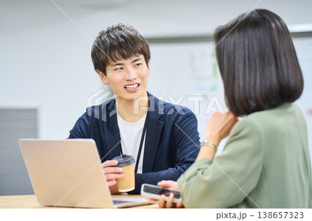 外資系オフィスで若い日本人ビジネスパーソンが笑顔で相談するワークスペース 138657323