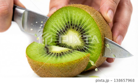 Close-up of a hand slicing a ripe kiwi fruit in half with a knife revealing its green interior and black seeds image highlights the preparation of a healthy and delicious fruit vitamin 138657968