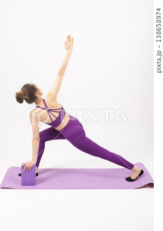 Fit woman in purple outfit using a block for yoga stretching Fit woman in purple outfit using a block for yoga stretching 138658974