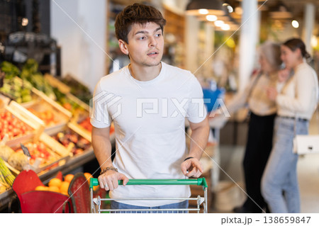 Young guy with shopping cart chooses groceries Young guy with shopping cart chooses groceries 138659847