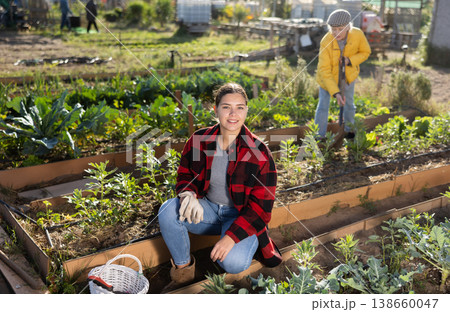 Smiling young female farmer posing with basket and garden instruments during season of sowing on sunny day of autumn Smiling young female farmer posing with basket and garden instruments during season of sowing on sunny day of autumn 138660047