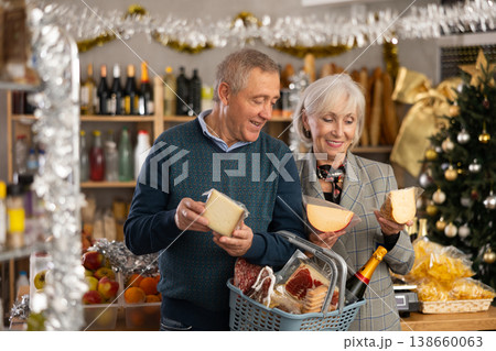 Elderly couple with a basket of groceries buys tasty cheese in grocery store 138660063