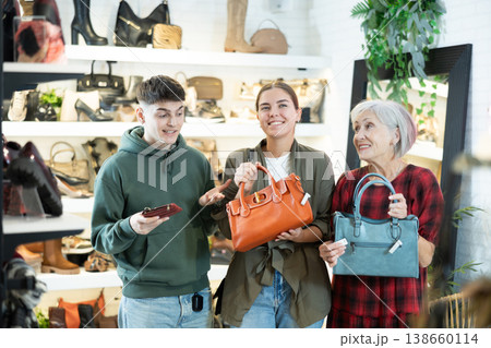 Mature woman sales consultant helps couple customers decide on choice of model handbag Mature woman sales consultant helps couple customers decide on choice of model handbag 138660114