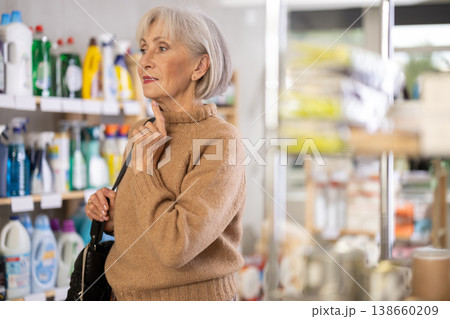 Elderly woman selects various household cleaning products for cleaning house Elderly woman selects various household cleaning products for cleaning house 138660209