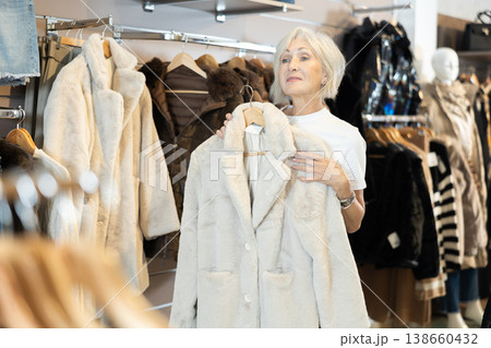 Old woman choosing white fur coat in clothing shop 138660432