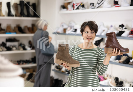 Adult woman chooses boots in shoe store Adult woman chooses boots in shoe store 138660481
